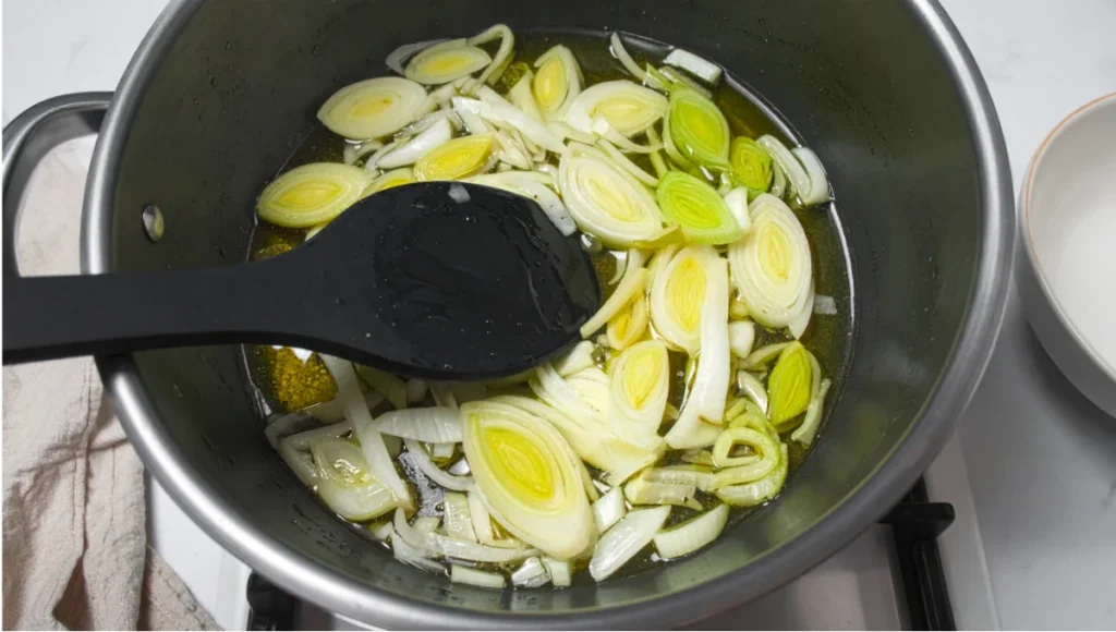 Thinly sliced leeks and onions sautéing in olive oil in a stainless steel pot during leek and potato soup preparation